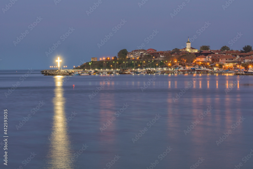 Lights of the UNESCO – protected ancient town of Nessebar at early night, reflecting on water. Church Assumption of the Holy Virgin in the far distance. Background. Tourism concept.