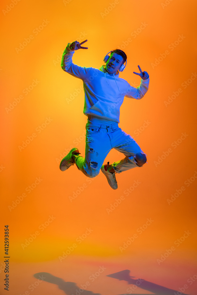 Flying. Caucasian man's portrait isolated on yellow studio background in mixed neon light. Listening music in headphones. Concept of human emotions, facial expression, sales, ad, fashion. Copyspace.