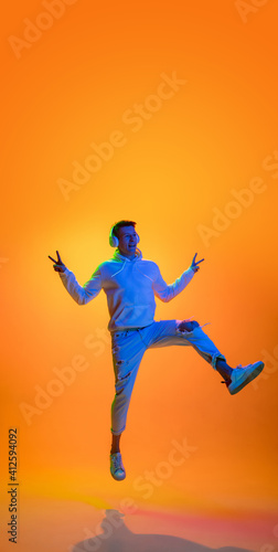Flying. Caucasian man's portrait isolated on yellow studio background in mixed neon light. Listening music in headphones. Concept of human emotions, facial expression, sales, ad, fashion. Copyspace.