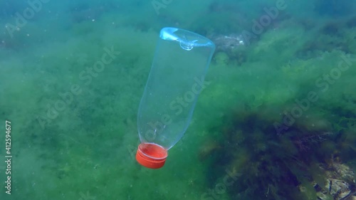 Plastic pollutio: PVC bottle slowly sinks to the bottom covered with algae, blue background. photo