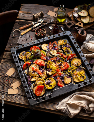 tasty baked slices of veggies (eggplants, tomatoes, pepper, onion, herbs) on baking tray on rustic wooden table