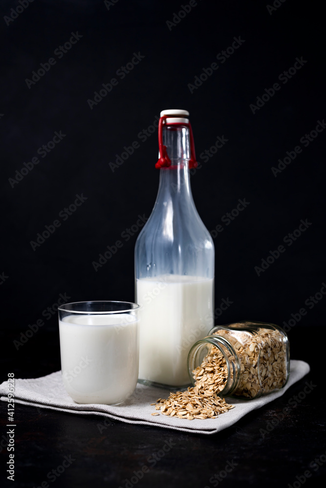 glass and bottle of vegetarian oatmeal milk on dark background glass and bottle of vegetarian oatmeal milk on dark background
