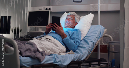 Aged male patient having video chat on digital tablet lying in hospital bed © nimito