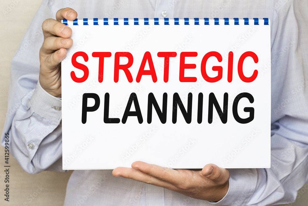 The businessman shows a sheet with the text SRATEGIC PLANNING on a white background. Business concept The businessman shows a sheet with the text SRATEGIC PLANNING on a white background. Business concept
