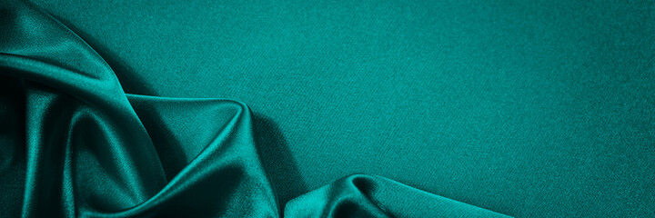Blue green silk satin background. Soft wavy folds on smooth, shiny fabric. Dark teal luxury background with copy space for design. Web banner.