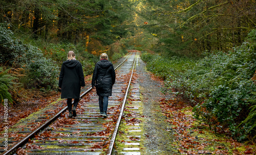 Rear view of a mother and daughter walking along a railway track in autumn, Goldstream, Vancouver Island, Canada photo