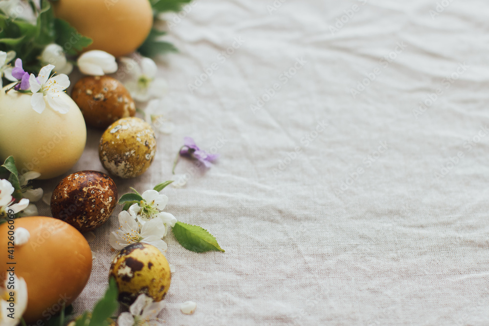 Happy Easter! Easter eggs with spring flowers on rustic linen, space for text. Aesthetic holiday