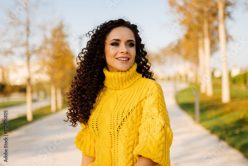 Smiling gentle smile girl in a bright sweater with curls of dark hair posing in the autumn park. High quality photo © mnelen.com