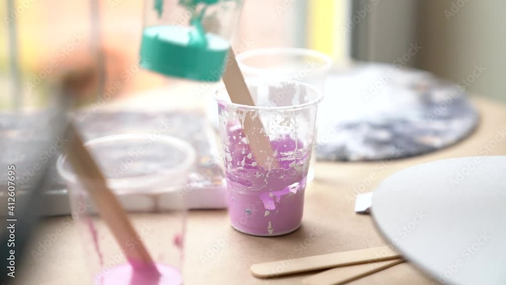 Closeup brushes, containers with mixed paints. Artist is creating picture, pouring color to canvas. Process of drawing, making abstract liquid acrylic painting in workshop. Fluid art therapy concept. Closeup brushes, containers with mixed paints. Artist is creating picture, pouring color to canvas. Process of drawing, making abstract liquid acrylic painting in workshop. Fluid art therapy concept.