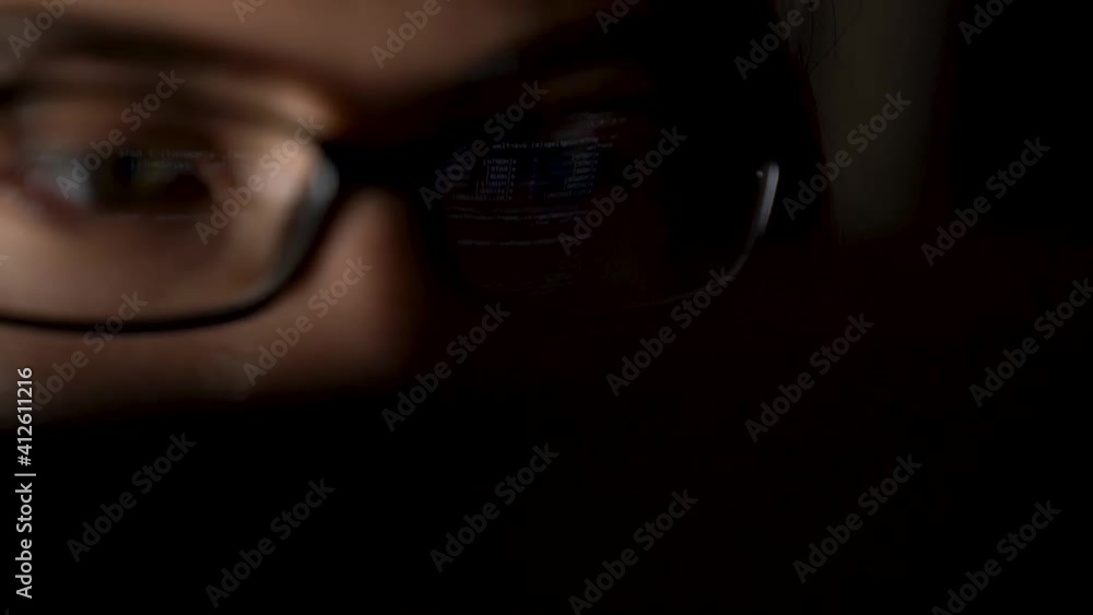 Closeup female eyes in glasses with screen reflection on lenses. Software developer freelancer woman is working with program code on workplace at night. Programmer girl develops web application. Closeup female eyes in glasses with screen reflection on lenses. Software developer freelancer woman is working with program code on workplace at night. Programmer girl develops web application.