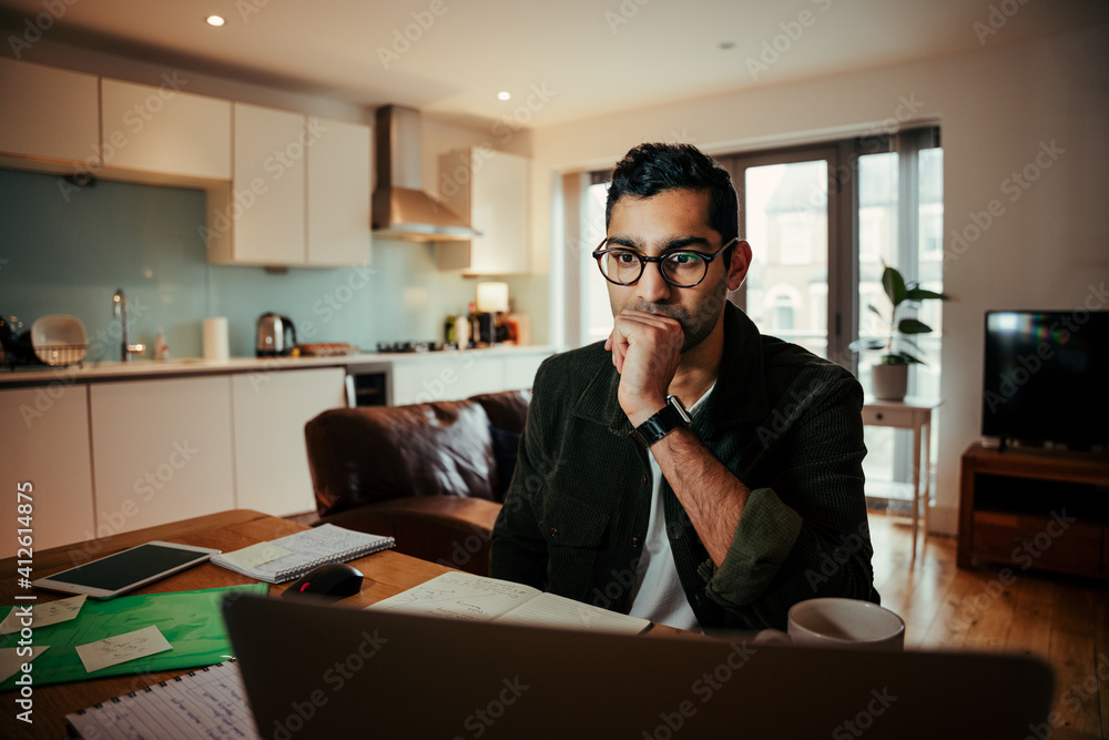 Mixed race businessman seated concentrating while working on laptop sitting at home office Mixed race businessman seated concentrating while working on laptop sitting at home office
