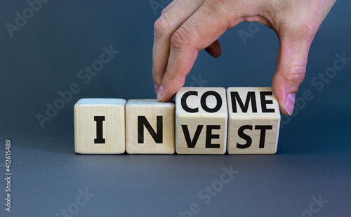 Invest or income symbol. Businessman turns wooden cubes and changes the word 'invest' to 'income'. Beautiful grey background, copy space. Business and invest or income concept.