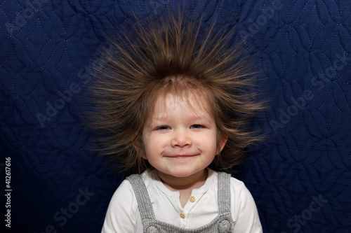 Portrait of a little smiling girl with electrified hair on a blue background.
Electricity power concept.