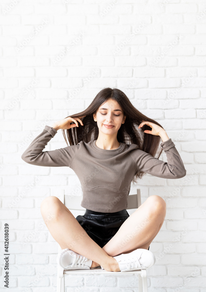 portrait of a beautiful brunette woman with long hair sitting on white brick wall background portrait of a beautiful brunette woman with long hair sitting on white brick wall background