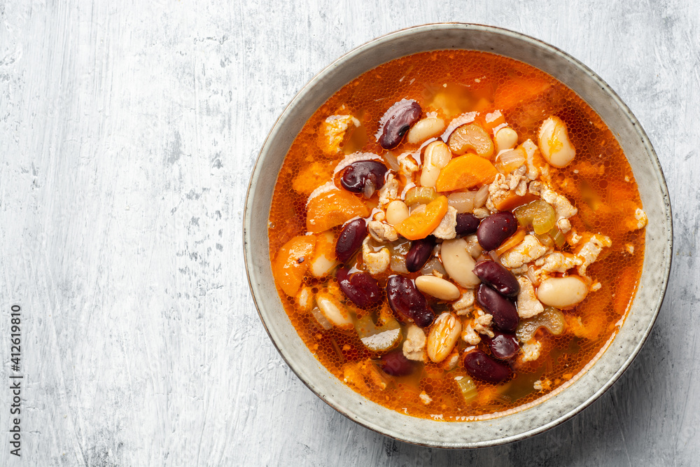Fototapeta premium Bean soup with bacon, carrot, celery and onion in bowl on concrete background
