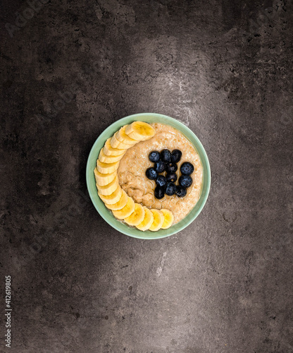 Bowl of oatmeal oatmeal with banana and blueberry on vintage table in flat gray weighted style. Healthy breakfast and diet food.