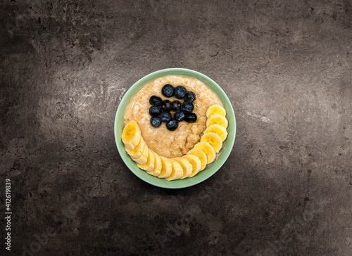 Bowl of oatmeal oatmeal with banana and blueberry on vintage table in flat gray weighted style. Healthy breakfast and diet food.