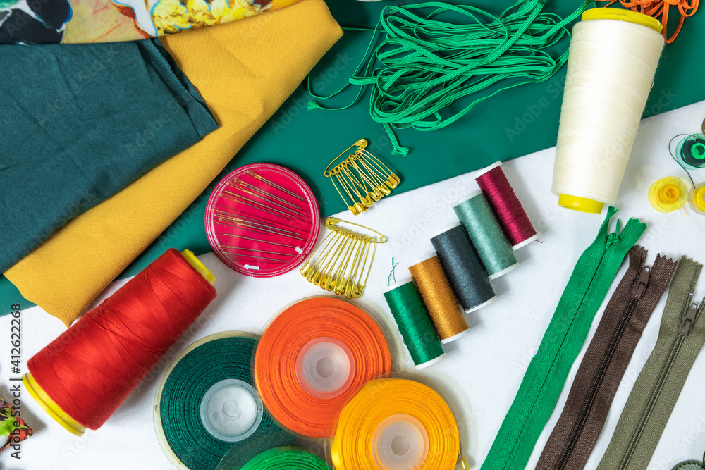 Fototapeta premium Dressmaker's workspace. Professional sewing material. Table with fabrics, elastic, safety pins, buttons, ribbons, zips, threads and needles. Top view