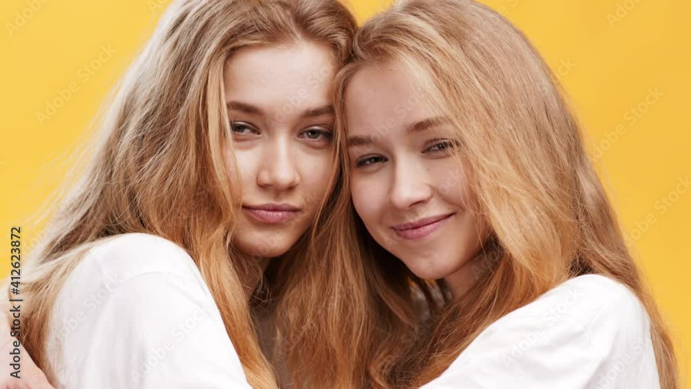 Sisters connection. Close up of two similar redhead twin ladies, embracing over orange studio background Sisters connection. Close up of two similar redhead twin ladies, embracing over orange studio background