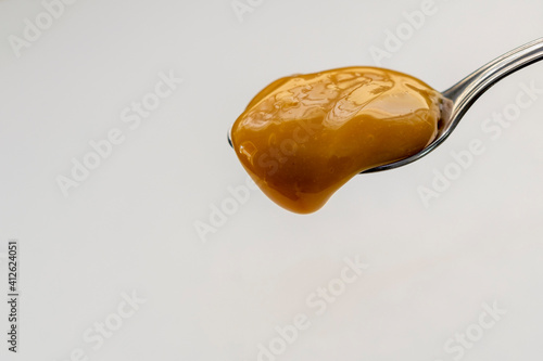 dulce de leche dripping from spoon, white background