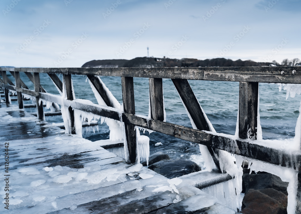 Frozen jetty at the ocean with huge icicles hanging at the wooden planks Frozen jetty at the ocean with huge icicles hanging at the wooden planks