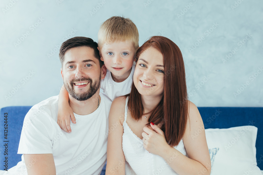Fototapeta premium Young family woman, husband and son having fun together in a large bedroom in the morning