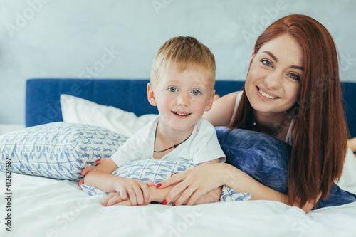 Young family woman, husband and son having fun together in a large bedroom in the morning