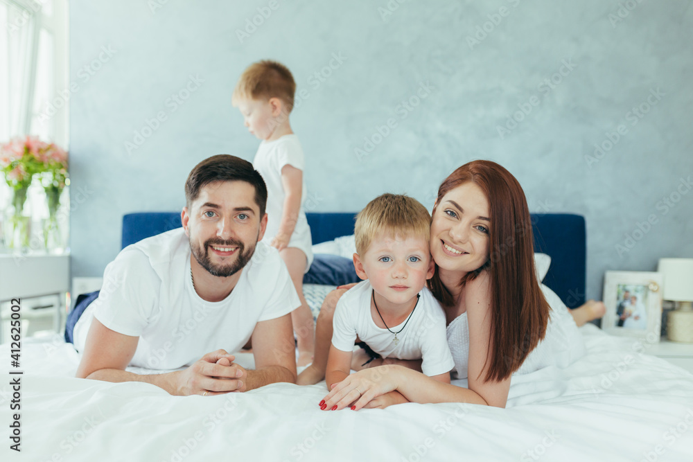 Young family husband wife and two young children, sons, have fun together in their bedroom