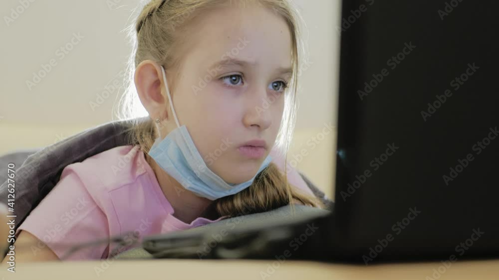 Cute girl wear protective masks and using laptop at home. Homeschooling, self-isolation, home quarantine. Technology, education, online learning, distance learning at home concept. Cute girl wear protective masks and using laptop at home. Homeschooling, self-isolation, home quarantine. Technology, education, online learning, distance learning at home concept.