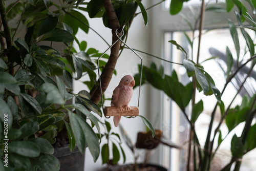 Small porcelain parrot sits in a swing, on a plant photo