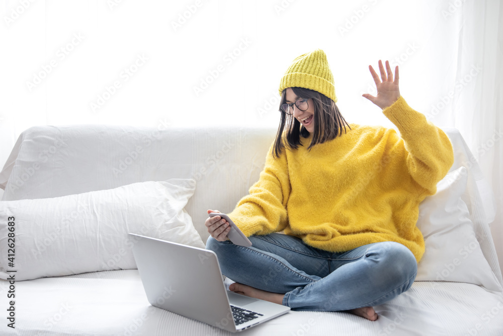 A young girl in a yellow sweater and yellow hat communicates via video call at home on the couch.