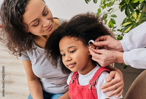 Hearing treatment for a child. African American girl with her mother during installation hearing aid by her audiologist