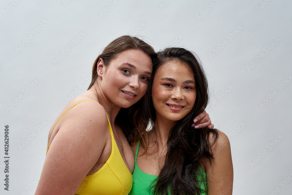 Portrait of two adorable young women with different body shapes wearing underwear smiling at camera while posing together isolated over light background Portrait of two adorable young women with different body shapes wearing underwear smiling at camera while posing together isolated over light background