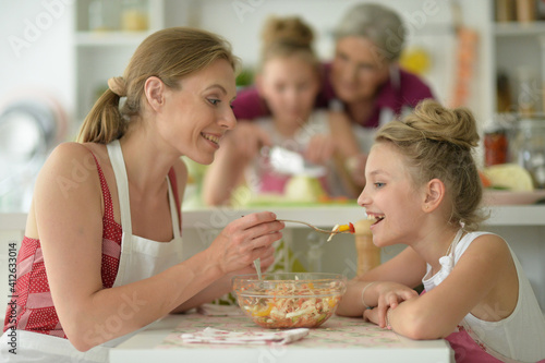 portrait of happy mother with daughter eating salad at home