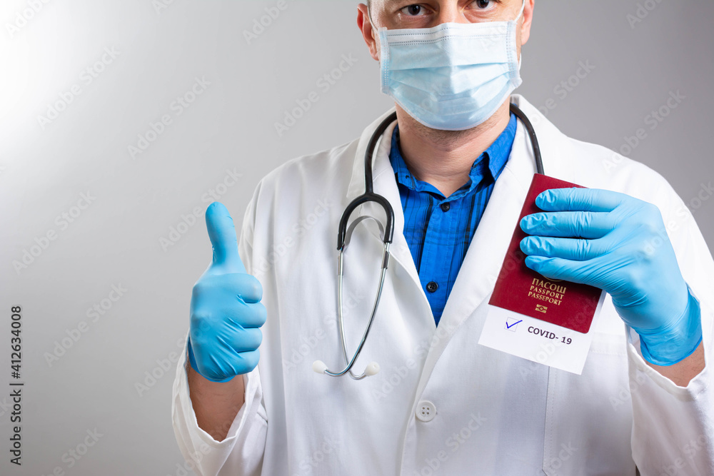 Concept of vaccination and digital passport. Hand in gloves shows thumb up and electronic Immunity passport with a COVID-19 vaccination stamp on a smartphone screen on the blue background. Flat lay.