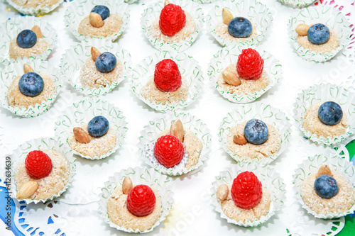 top view of dessert with coconut, ripe berries, almonds, raspberries and blueberries. In a white paper wrapper with green hearts