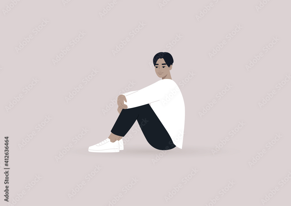 Obraz premium A young male Asian character sitting on the floor and hugging their knees, casual daily life scene