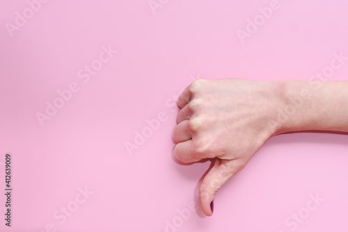 Hand of a caucasian young woman doing gesture of thumbs down on a pink background