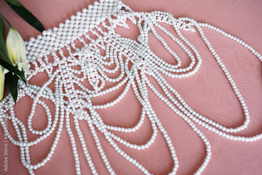 Fototapeta premium White lilies with green leaves and a necklace of pearls on a pink background. Selective focus