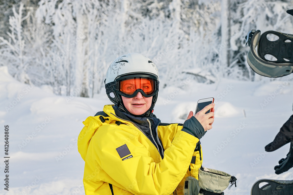 Woman snowboarder in bright suit in a sports helmet photographed on a smartphone. Extreme sports. Leisure activity. Looking at camera