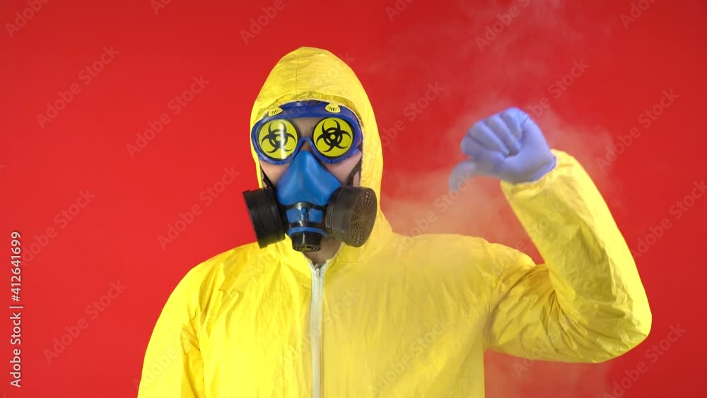 A Man in a Protective Yellow Suit and in a Protective Mask Shows a Finger Down, the Sign Does Not Like. Protection Concept, Radioactive Hazard Concept. Red background, isolate, studio footage, 4k. A Man in a Protective Yellow Suit and in a Protective Mask Shows a Finger Down, the Sign Does Not Like. Protection Concept, Radioactive Hazard Concept. Red background, isolate, studio footage, 4k.
