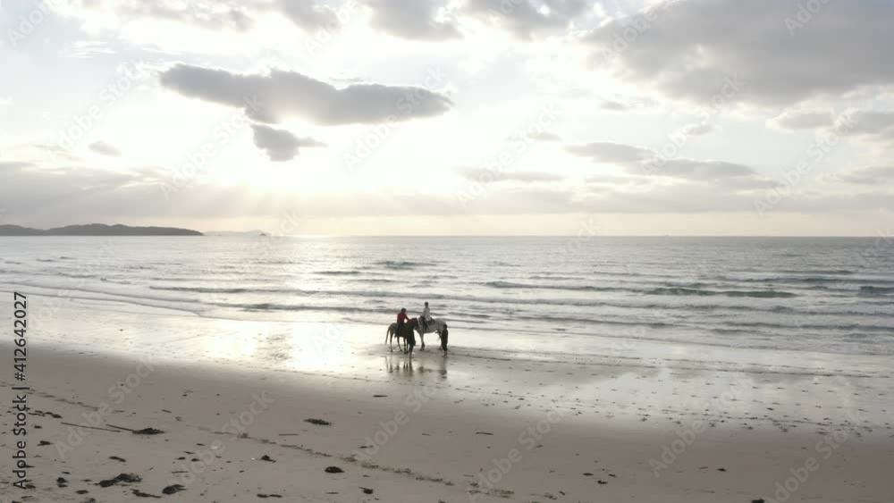 A couple riding a horse on the sandy beach at sunset A couple riding a horse on the sandy beach at sunset