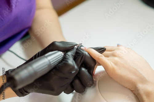 Manicurist in protective gloves applies nail polish to a woman s nails in a beauty salon. Professional manicure in a nail studio  photo of the process 