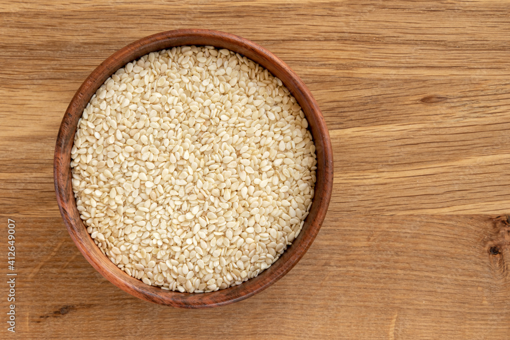 White sesame seeds in a bowl, isolated on wooden background. White sesame seeds in a bowl, isolated on wooden background.