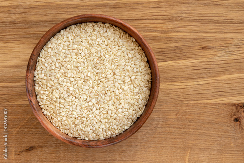 White sesame seeds in a bowl, isolated on wooden background. photo