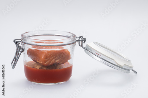 Clear glass jar with tomato gel and baked salmon on white background