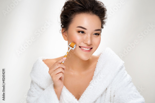 Beautiful woman using derma roller for her facial skin. Photo of asian woman after shower on white background. Beauty and skin care concept photo