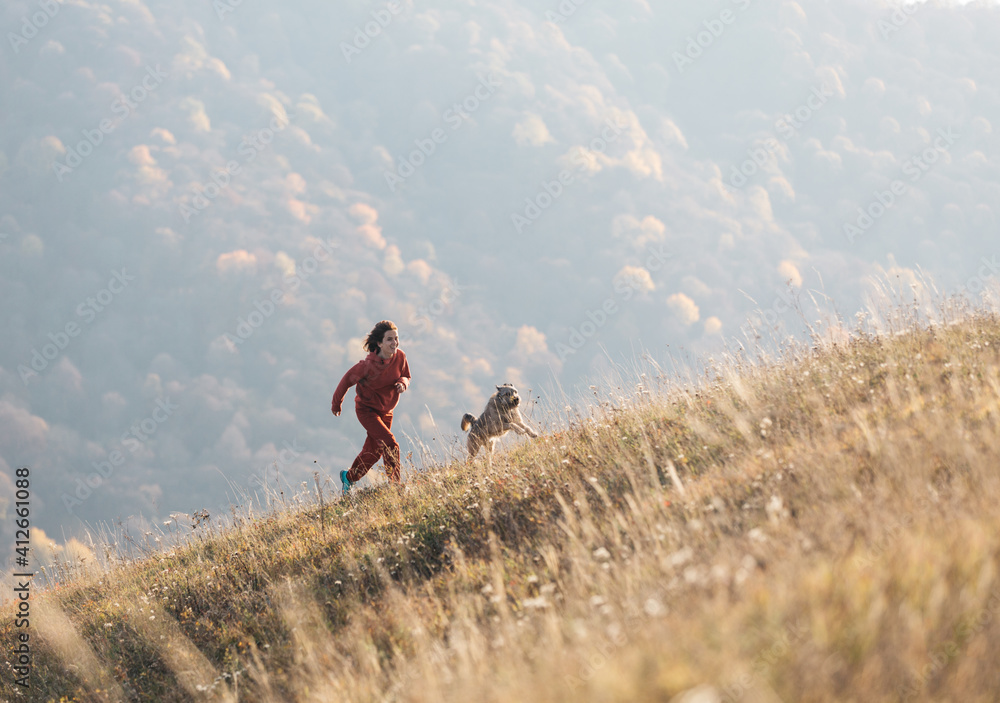 cheerful woman walks with her dog. They run uphill at dawn in the sunlight.