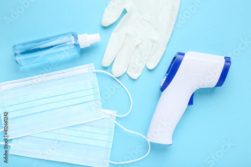 Medical masks, gloves, sanitizer bottle and infrared thermometer on blue background