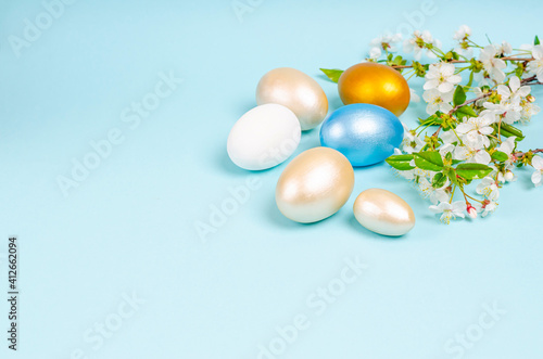 Easter painted mother-of-pearl eggs with cherry blossoms on a blue background with copy space.